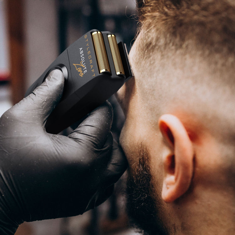 A close-up of a black beard trimmer with gold-colored blades being used by a person wearing a black glove. The brand name 'AIRDUTY' is clearly visible on the trimmer.