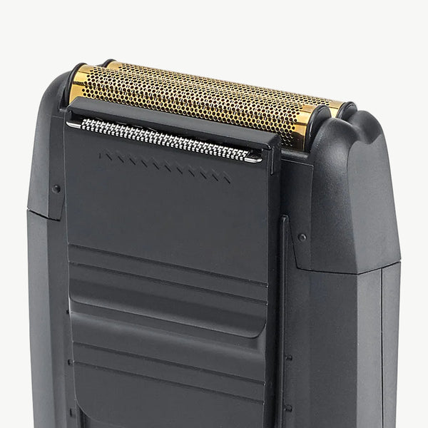 Close-up of a black electric shaver showing the top shaving head with a gold-toned mesh filter and silver blade edge, set against a plain light gray background.