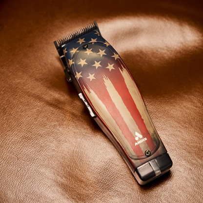 Andis Master 1776 cordless clipper laying on rich leather surface, luxury barber tool photography