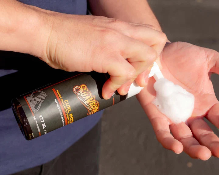 Person applying a white substance from a bottle labeled 'Curl Mousse' to their hand.